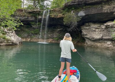 A person standing on a paddleboard near a small waterfall