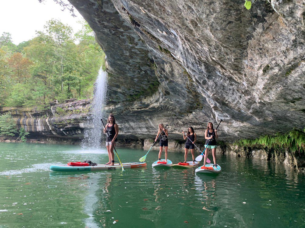 Four women standing on paddleboards under a cave